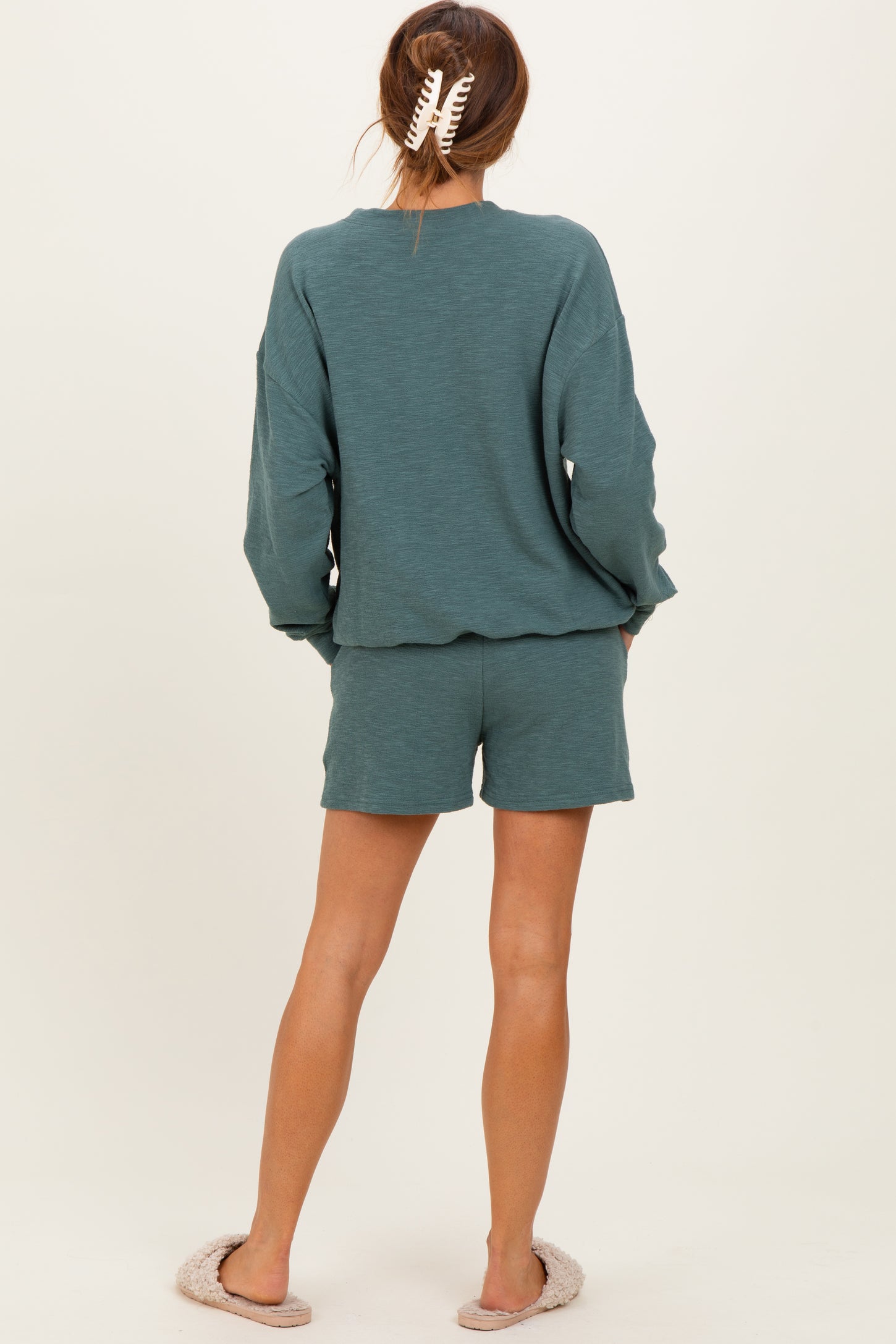 woman wearing a teal long sleeve top and matching shorts, showing the back with casual slippers on