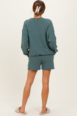 woman wearing a teal long sleeve top and matching shorts, showing the back with casual slippers on