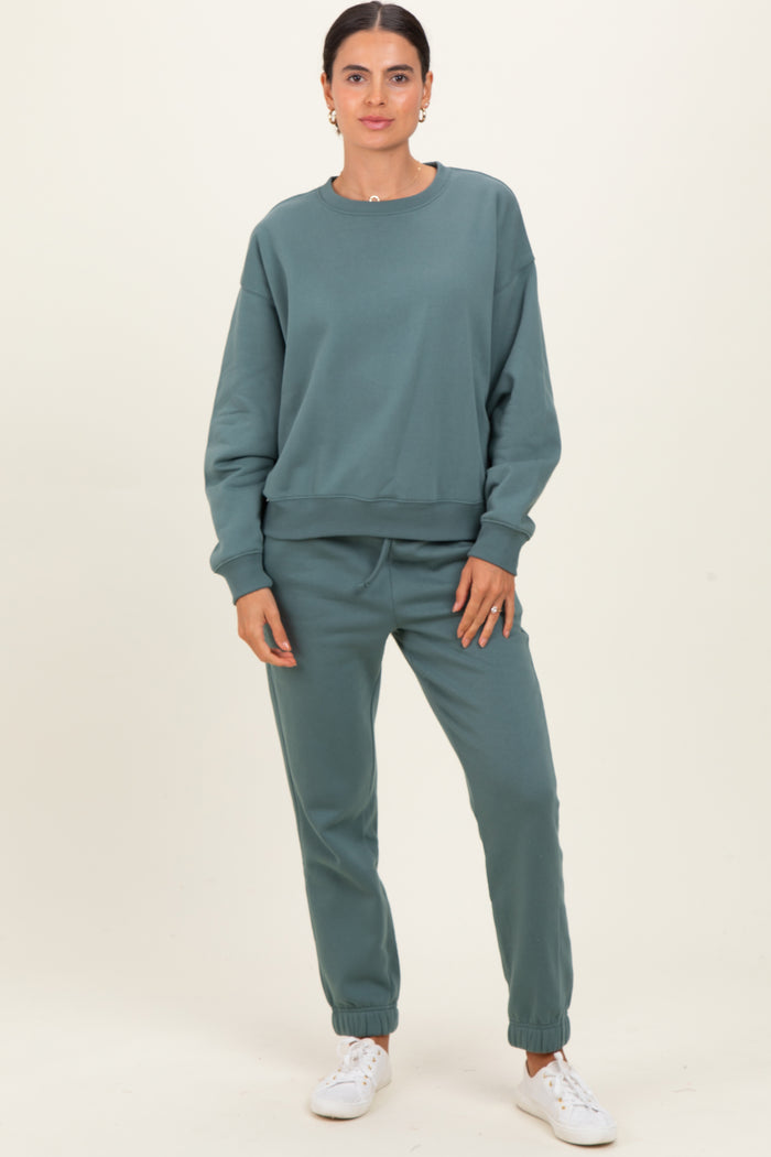 woman wearing a teal oversized sweatshirt and matching jogger pants, standing against a neutral background