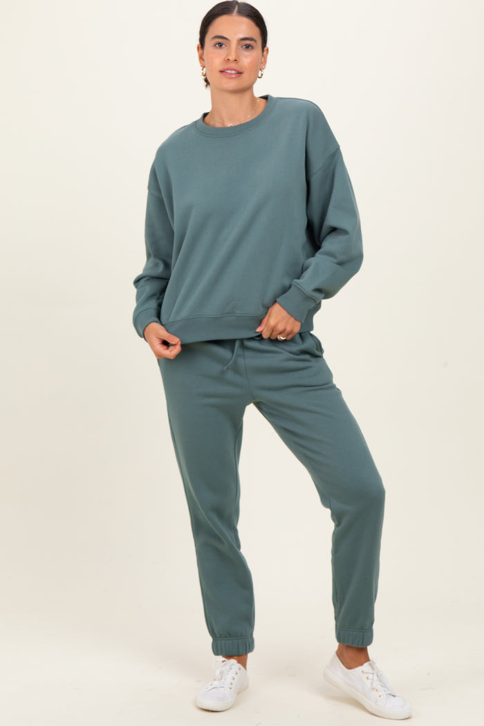 woman wearing a green long sleeve sweatshirt and matching sweatpants, standing with one hand on her hip