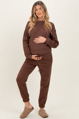 woman wearing a brown maternity loungewear set with a sweatshirt and jogger pants, holding her baby bump