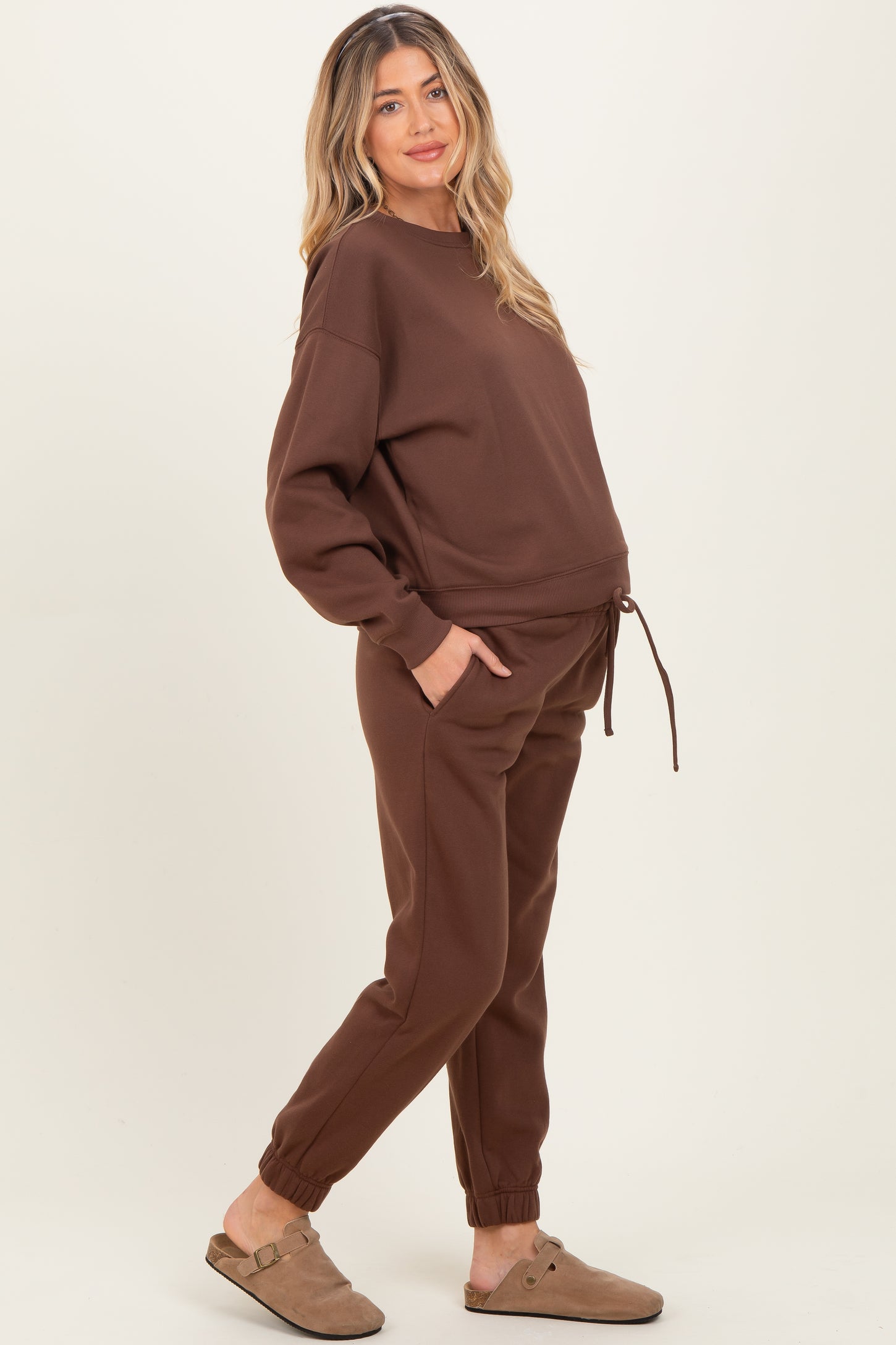 woman wearing a brown maternity sweatshirt and matching joggers with a drawstring, showing a baby bump