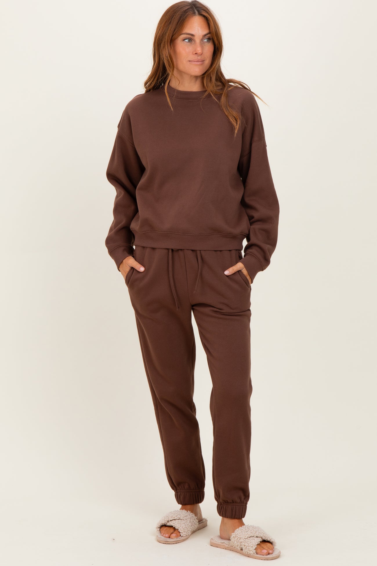 woman wearing a brown sweatshirt and matching jogger pants with pockets, styled with cozy slippers