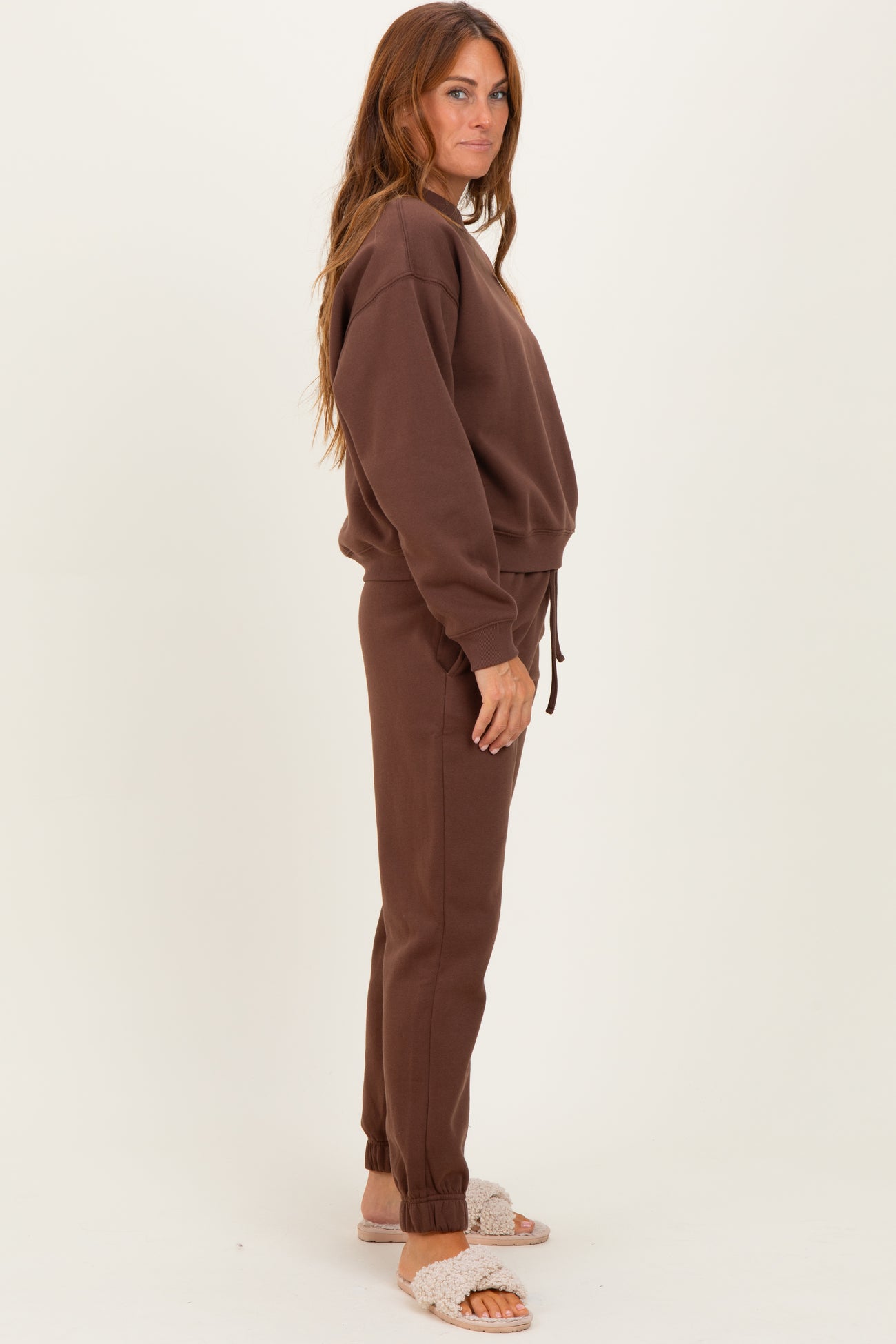 woman wearing a brown sweatshirt and matching sweatpants, styled with light-colored slippers