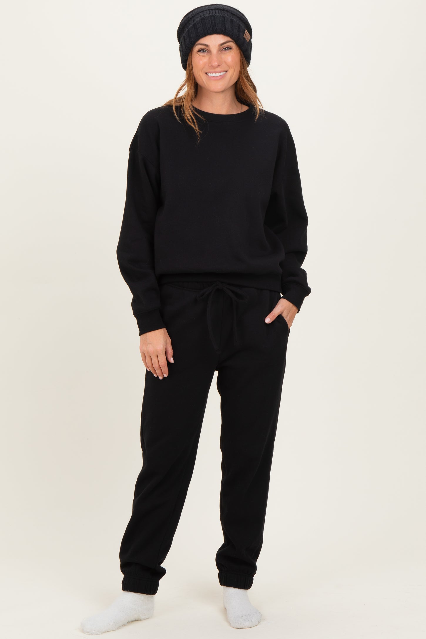 woman wearing a black sweatshirt and black jogger pants, styled with a beanie and cozy socks, standing casually