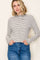 woman wearing a cream and black striped long sleeve top with a mock neck and slim fit, paired with high-waisted blue jeans