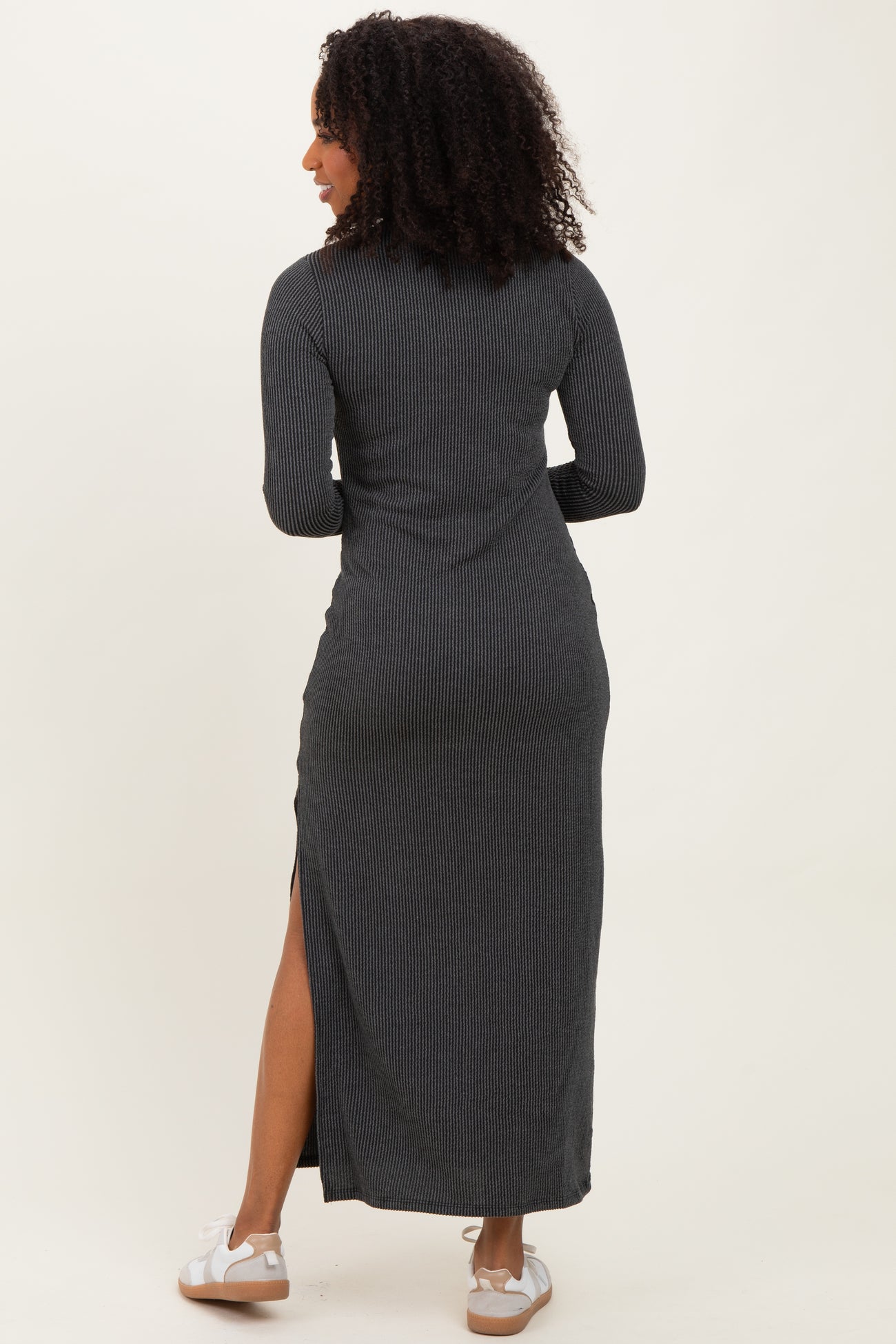 woman wearing a black ribbed maxi dress with long sleeves and a side slit, facing away from the camera