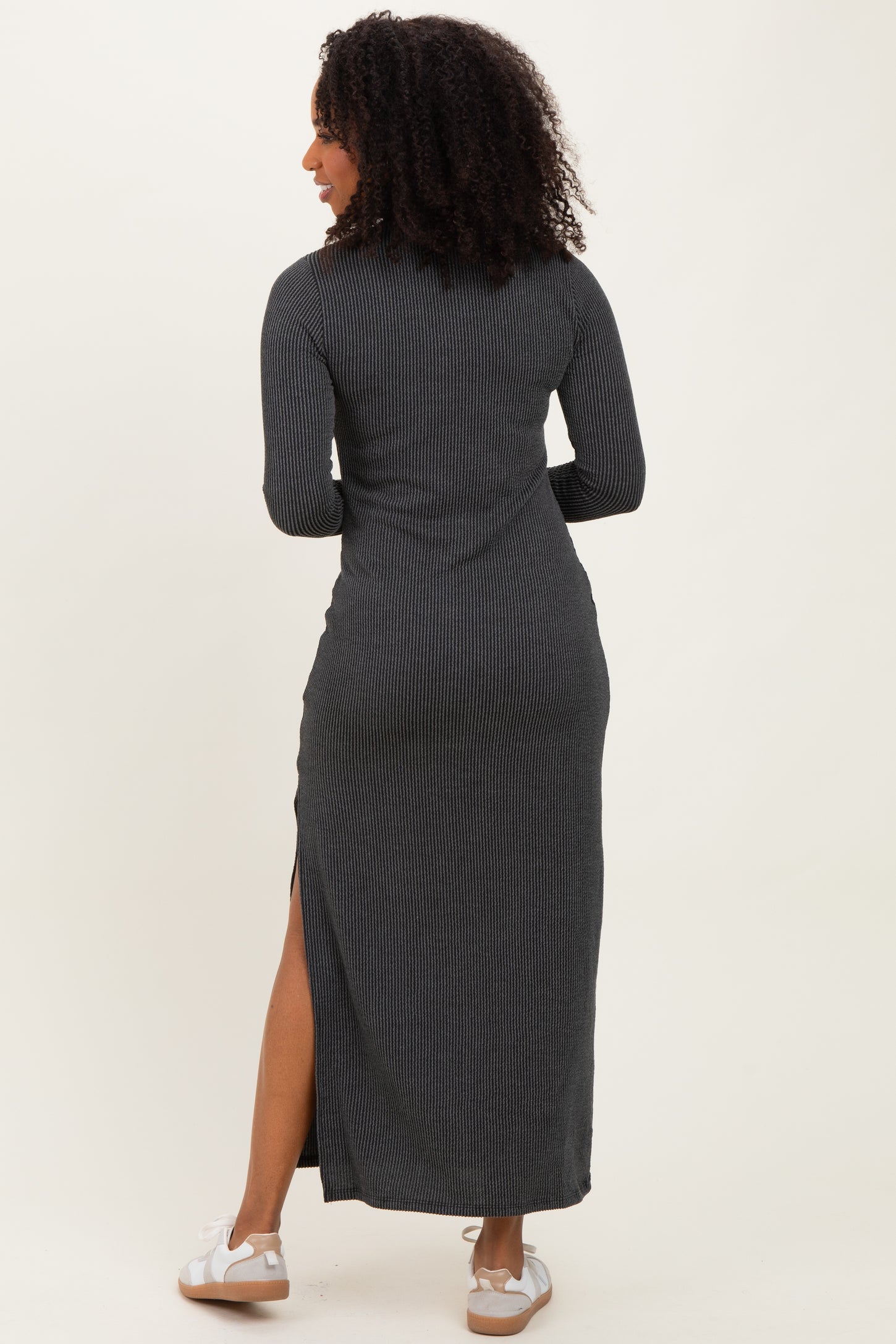 woman wearing a black ribbed maxi dress with long sleeves and a side slit, facing away from the camera