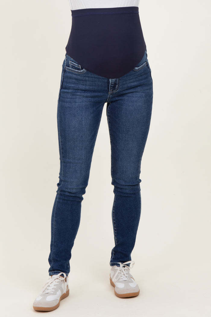 woman wearing navy blue maternity skinny jeans with a high waistband, paired with white athletic shoes