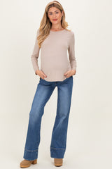 woman wearing a beige long sleeve maternity top and blue flared jeans, showing her baby bump