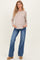 woman wearing a beige long sleeve maternity top and blue flared jeans, showing her baby bump