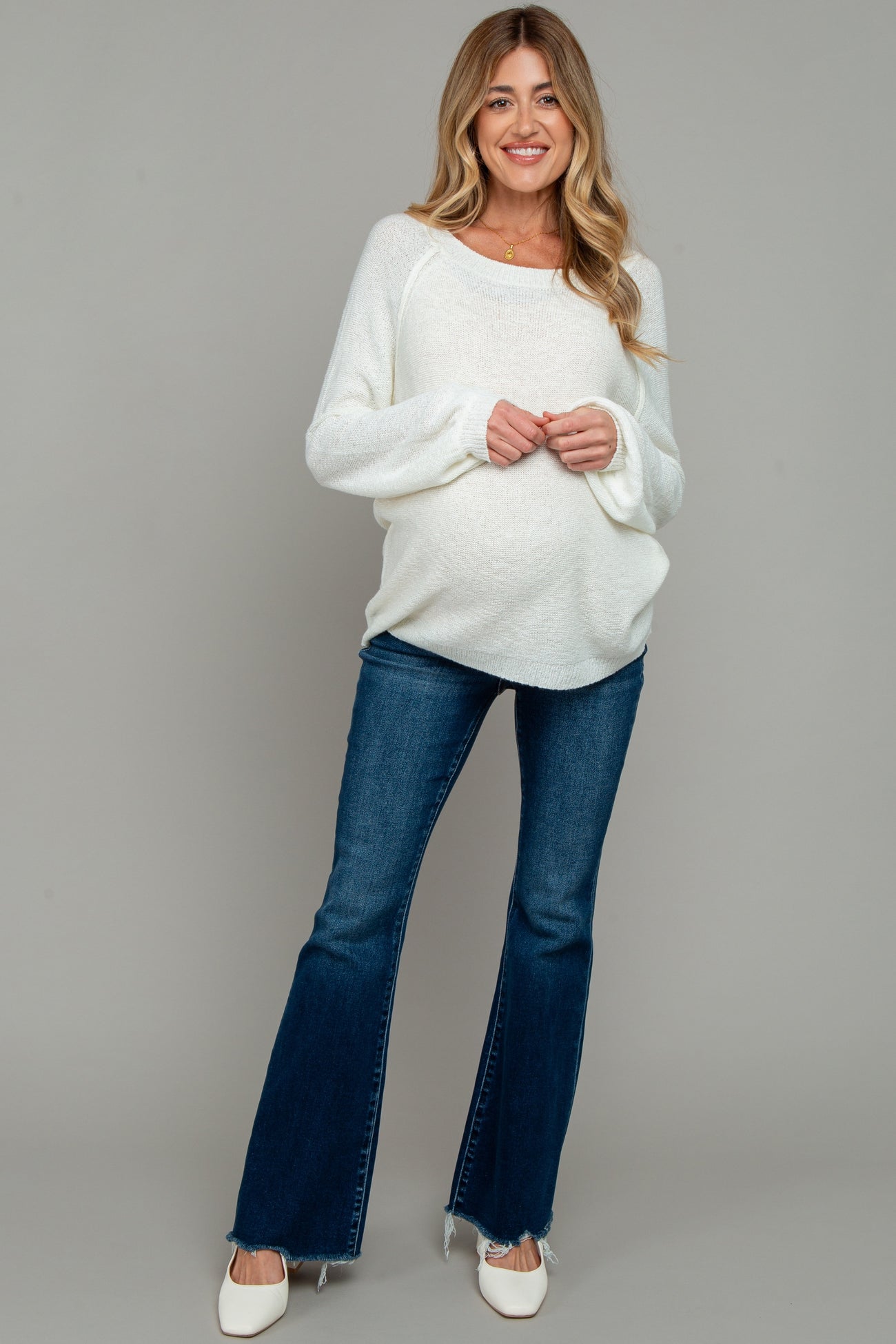 woman wearing a white long sleeve maternity sweater and blue flared jeans, showing her baby bump