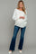 woman wearing a white long sleeve maternity sweater and blue flared jeans, showing her baby bump
