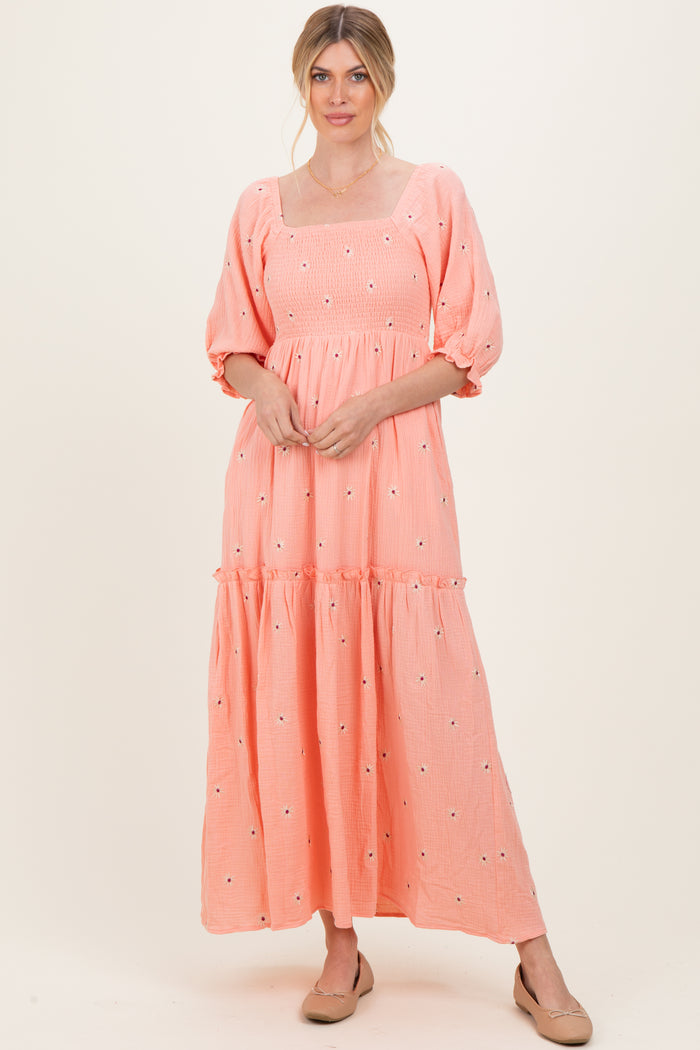 woman wearing a peach puff sleeve maxi dress with floral embroidery and a tiered skirt