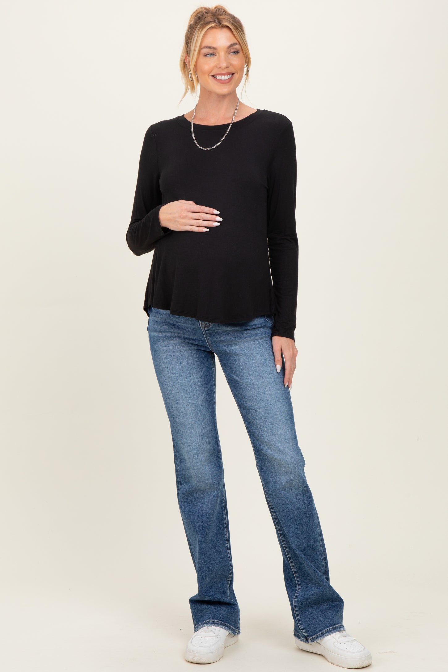 woman wearing a black long sleeve maternity top and blue jeans, holding her baby bump