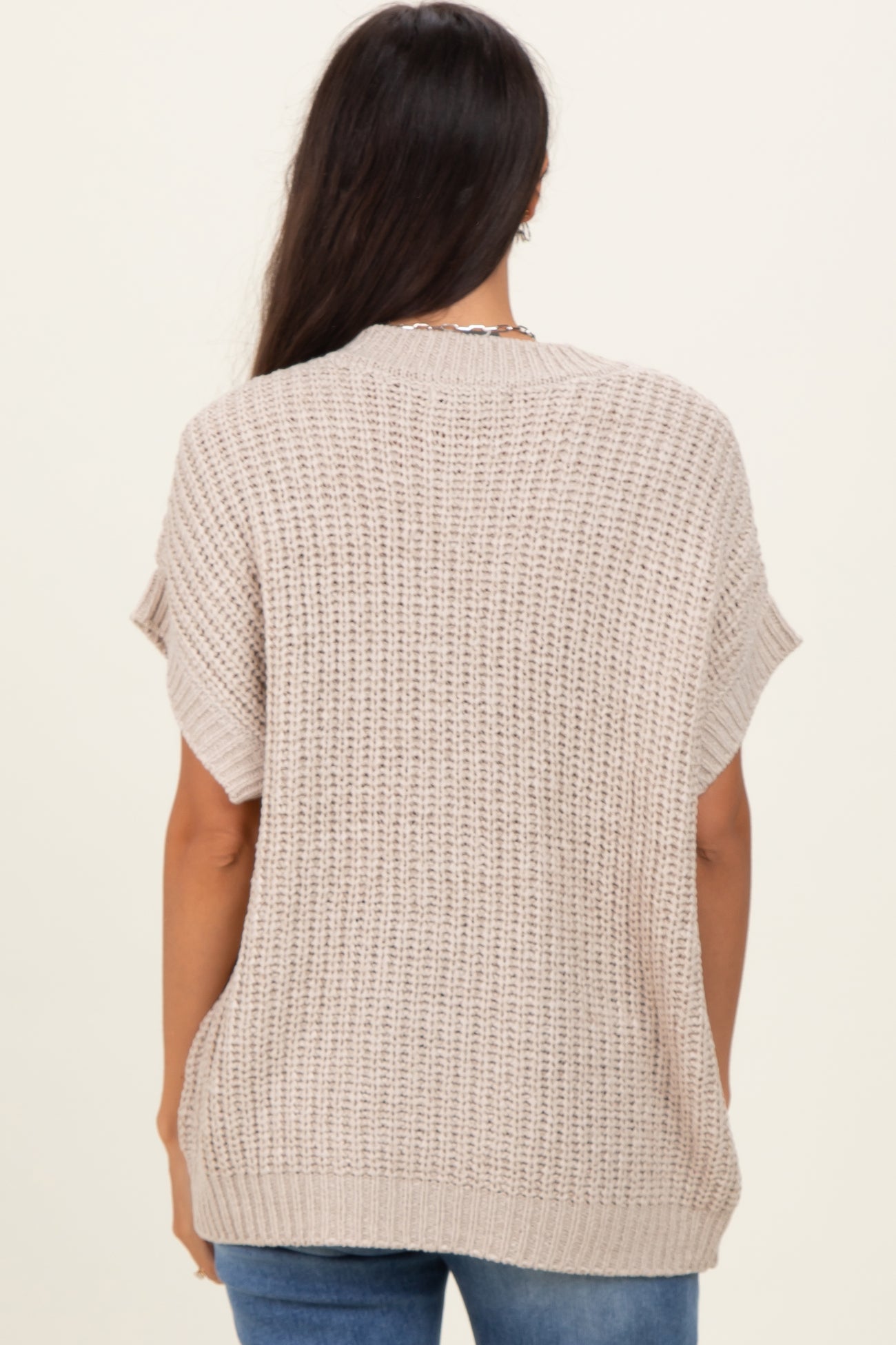 woman wearing a beige knitted oversized sweater from the back, paired with blue jeans