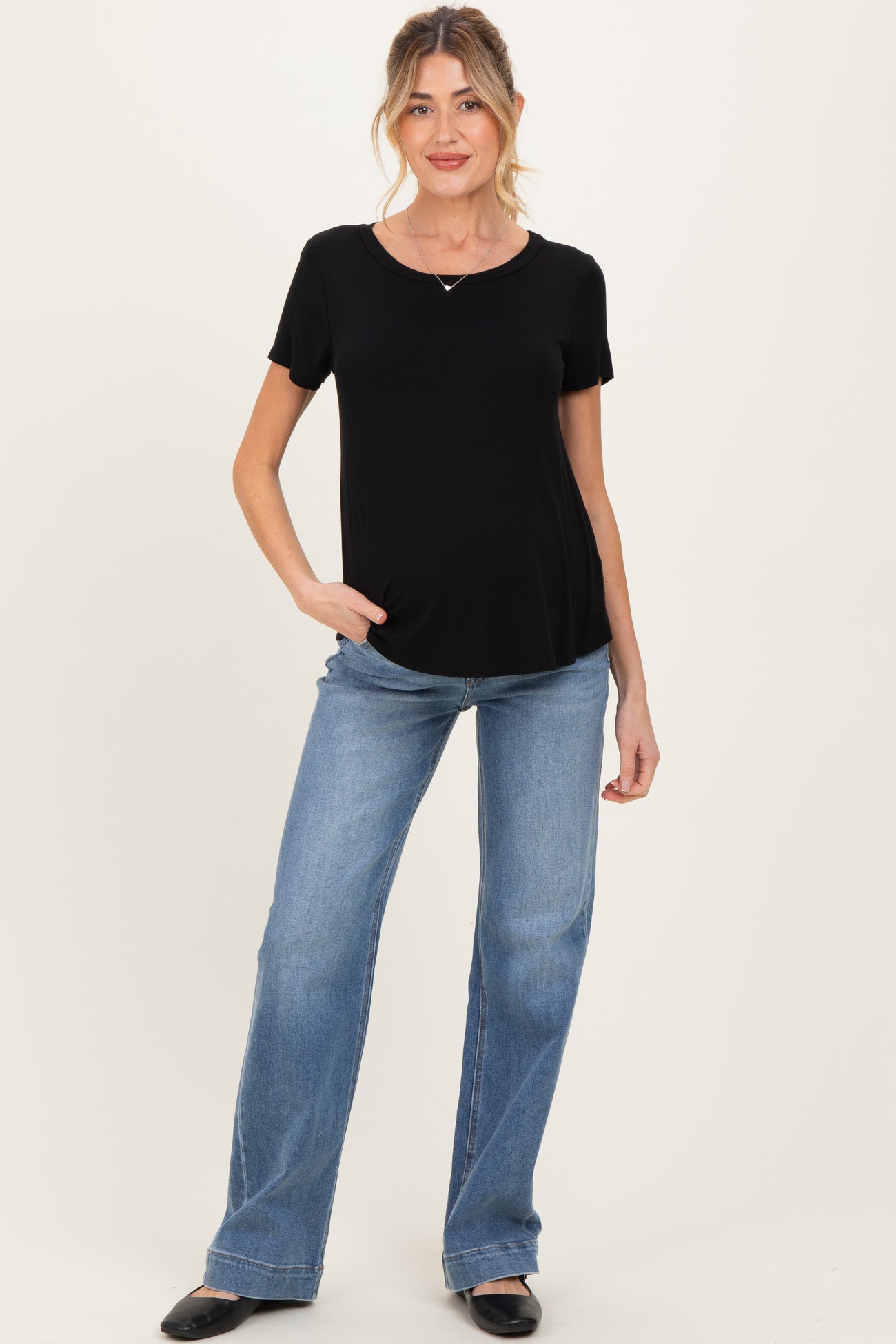 woman wearing a black short sleeve maternity top and light blue flared jeans, posing hands in pockets