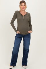 woman wearing an olive green maternity long sleeve henley top and blue jeans, showing her baby bump