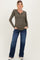 woman wearing an olive green maternity long sleeve henley top and blue jeans, showing her baby bump