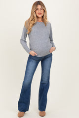 woman wearing a gray maternity sweater with a baby bump and flared blue jeans, posing with hands in pockets
