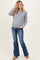 woman wearing a gray maternity sweater and blue flared jeans, with a slight baby bump visible, adjusting her glasses