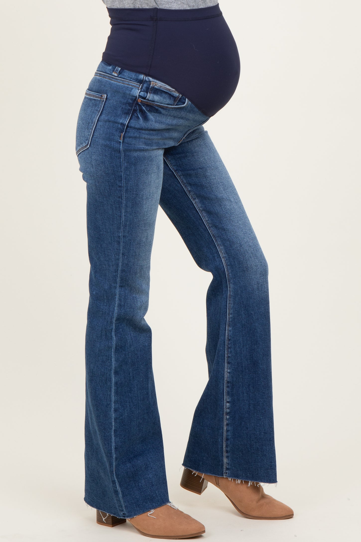 woman wearing blue maternity flared jeans with a dark waistband, showing her baby bump while standing sideways