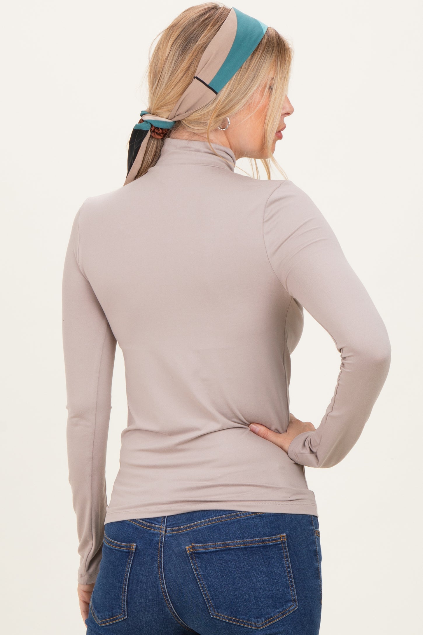 woman wearing a taupe long sleeve mock neck top paired with blue jeans, view from the back