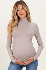 woman wearing a taupe long sleeve maternity top with a fitted turtleneck and holding her baby bump