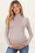 woman wearing a taupe long sleeve maternity top with a fitted turtleneck and holding her baby bump