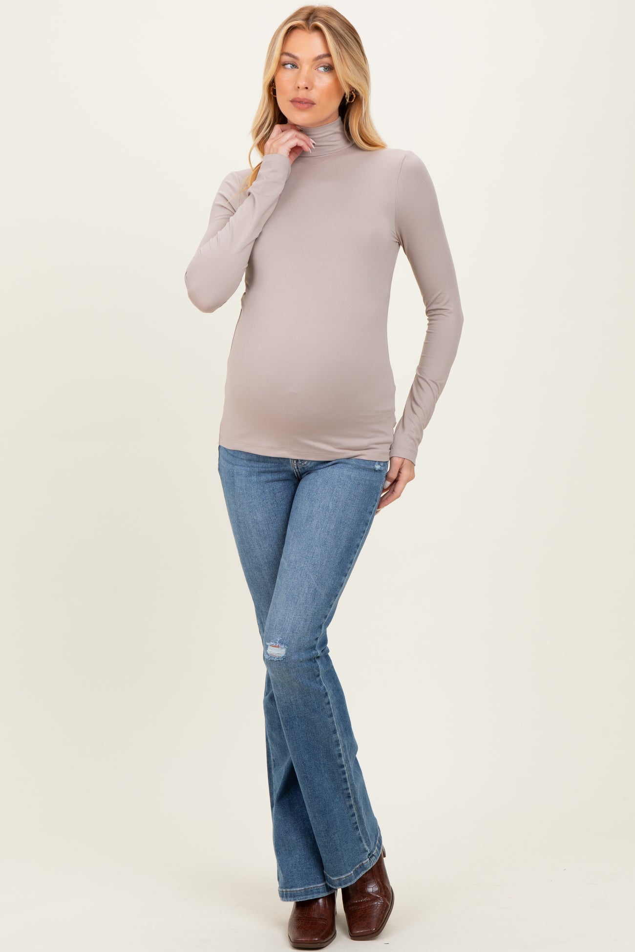 woman wearing a taupe long sleeve maternity top and blue flared jeans, showing her baby bump