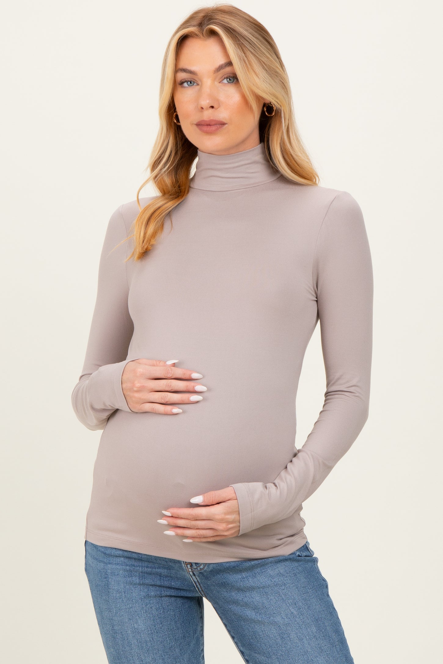woman wearing a taupe long sleeve maternity turtleneck top and holding her baby bump