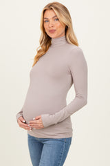 woman wearing a light taupe long sleeve maternity top and holding her baby bump