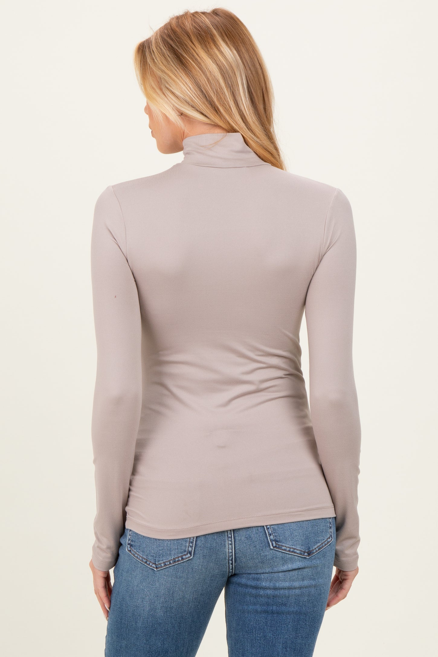 woman wearing a taupe long sleeve maternity top with a mock neck, viewed from the back