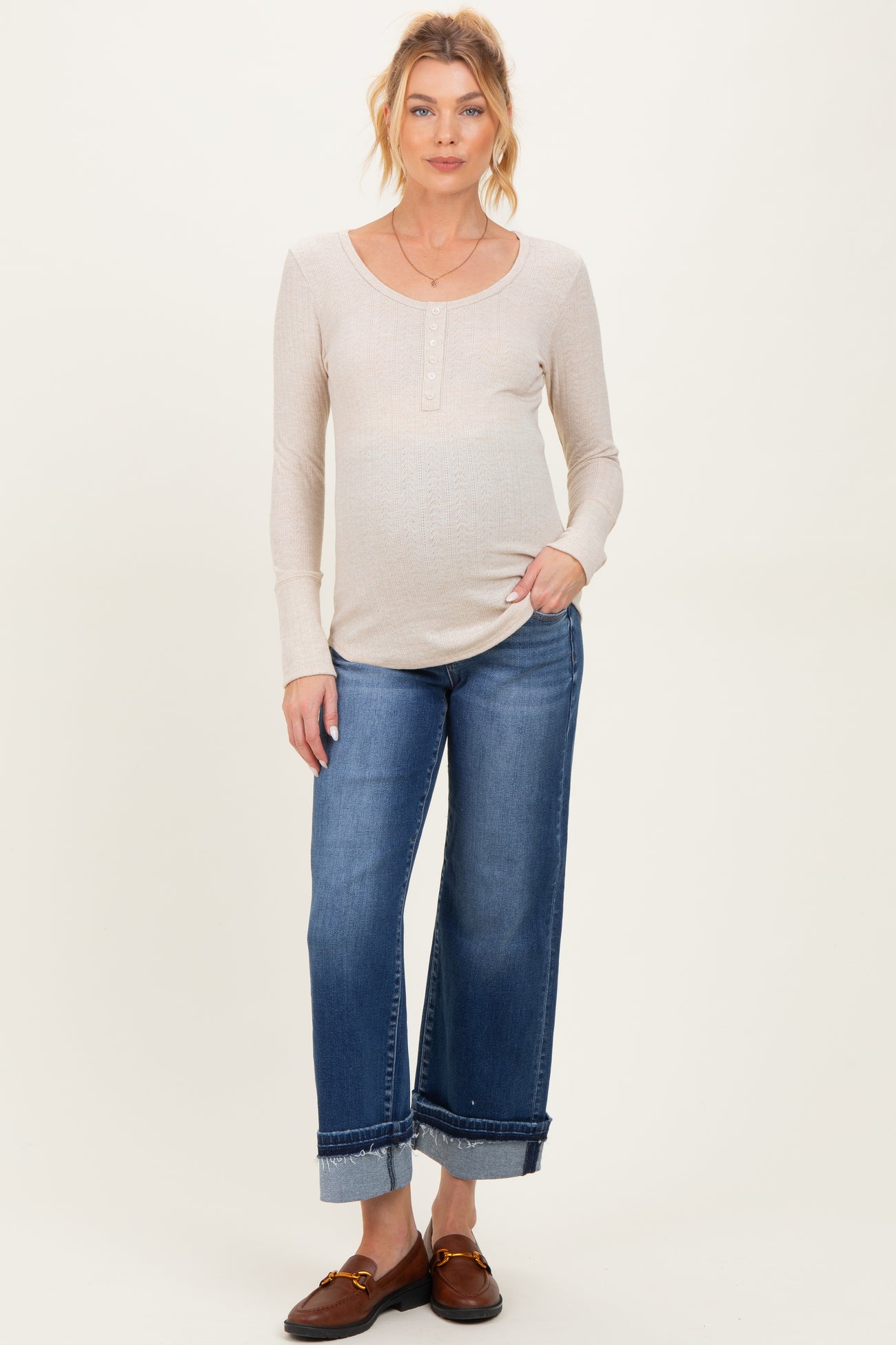woman wearing a beige scoop neck maternity top and blue wide-leg jeans, showcasing her baby bump