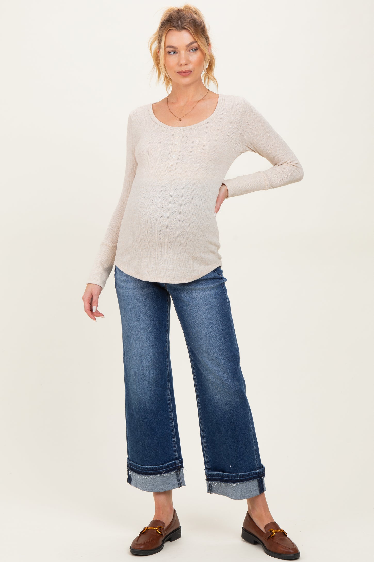 woman wearing a beige long sleeve maternity top and blue wide-leg jeans, showing her baby bump