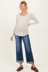 woman wearing a beige long sleeve maternity top and blue wide-leg jeans, showing her baby bump