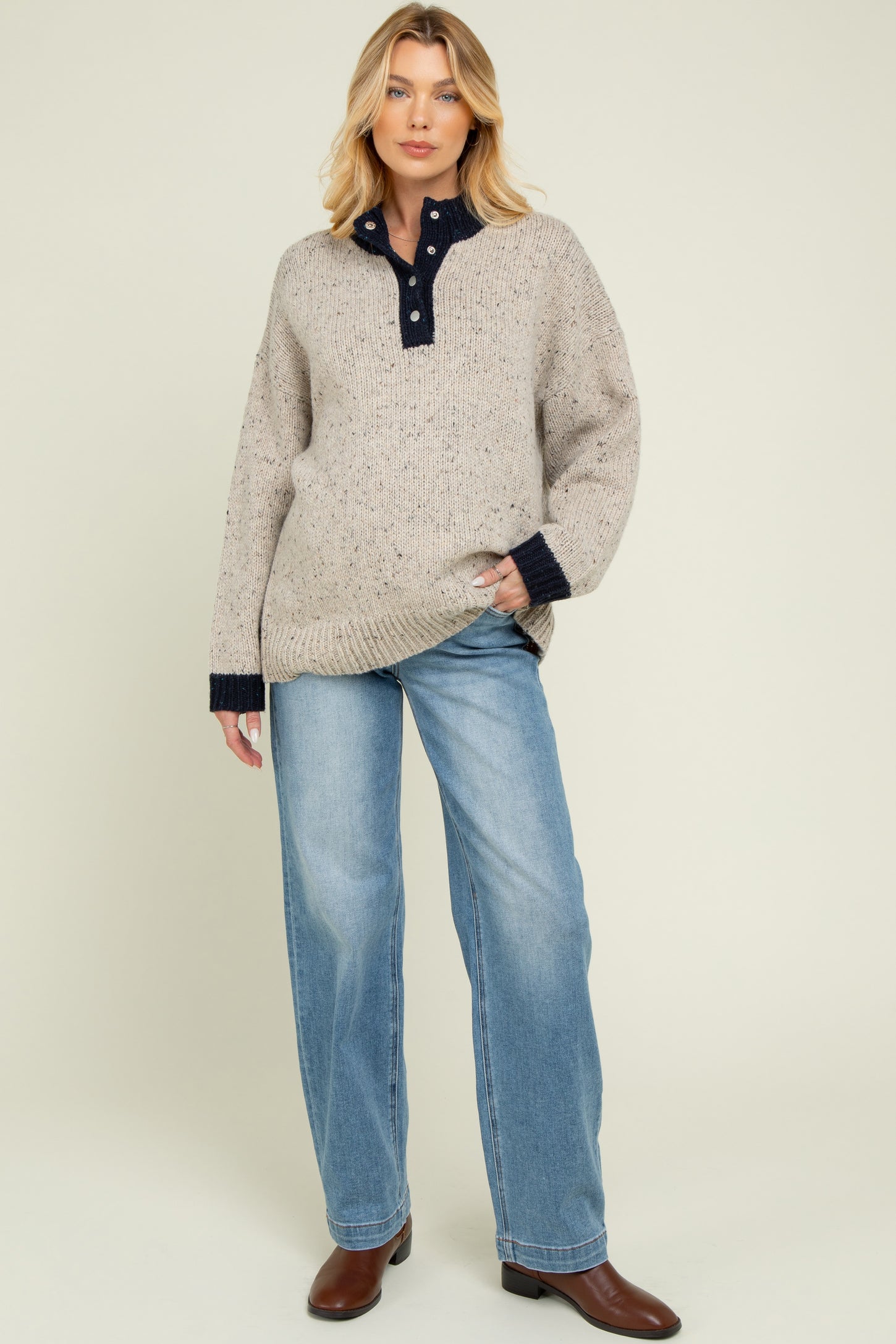 woman wearing a beige maternity sweater with navy collar and cuffs, paired with light blue maternity jeans