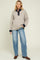 woman wearing a beige maternity sweater with navy collar and cuffs, paired with light blue maternity jeans