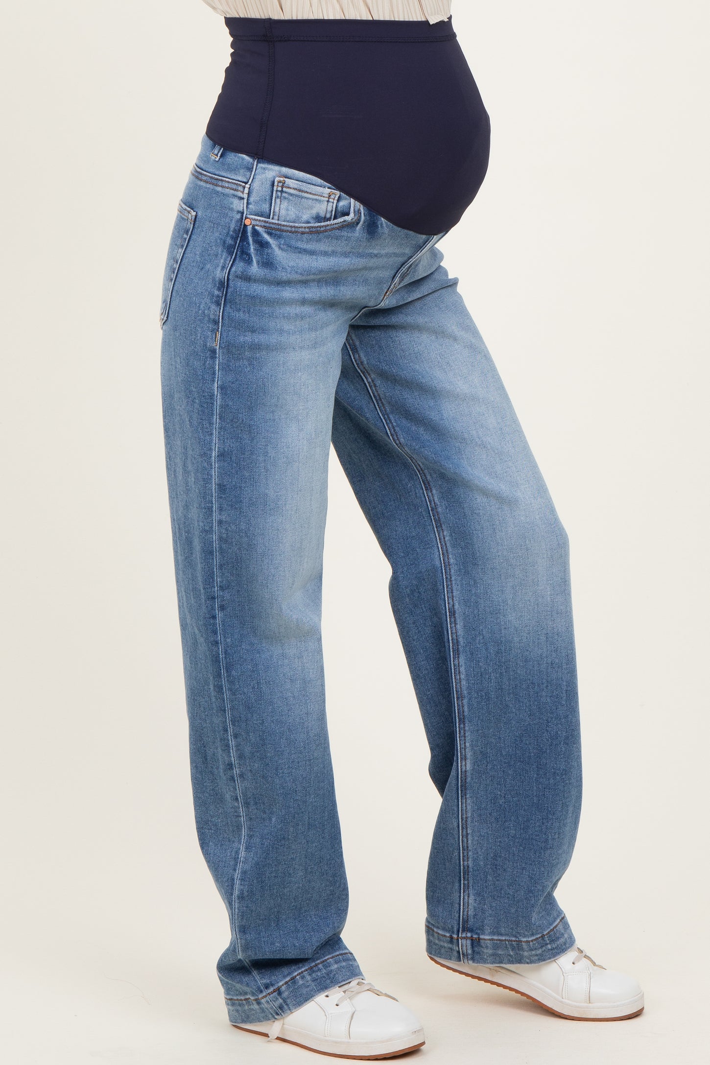 woman wearing a pair of light blue maternity jeans with a navy blue belly panel and a visible baby bump