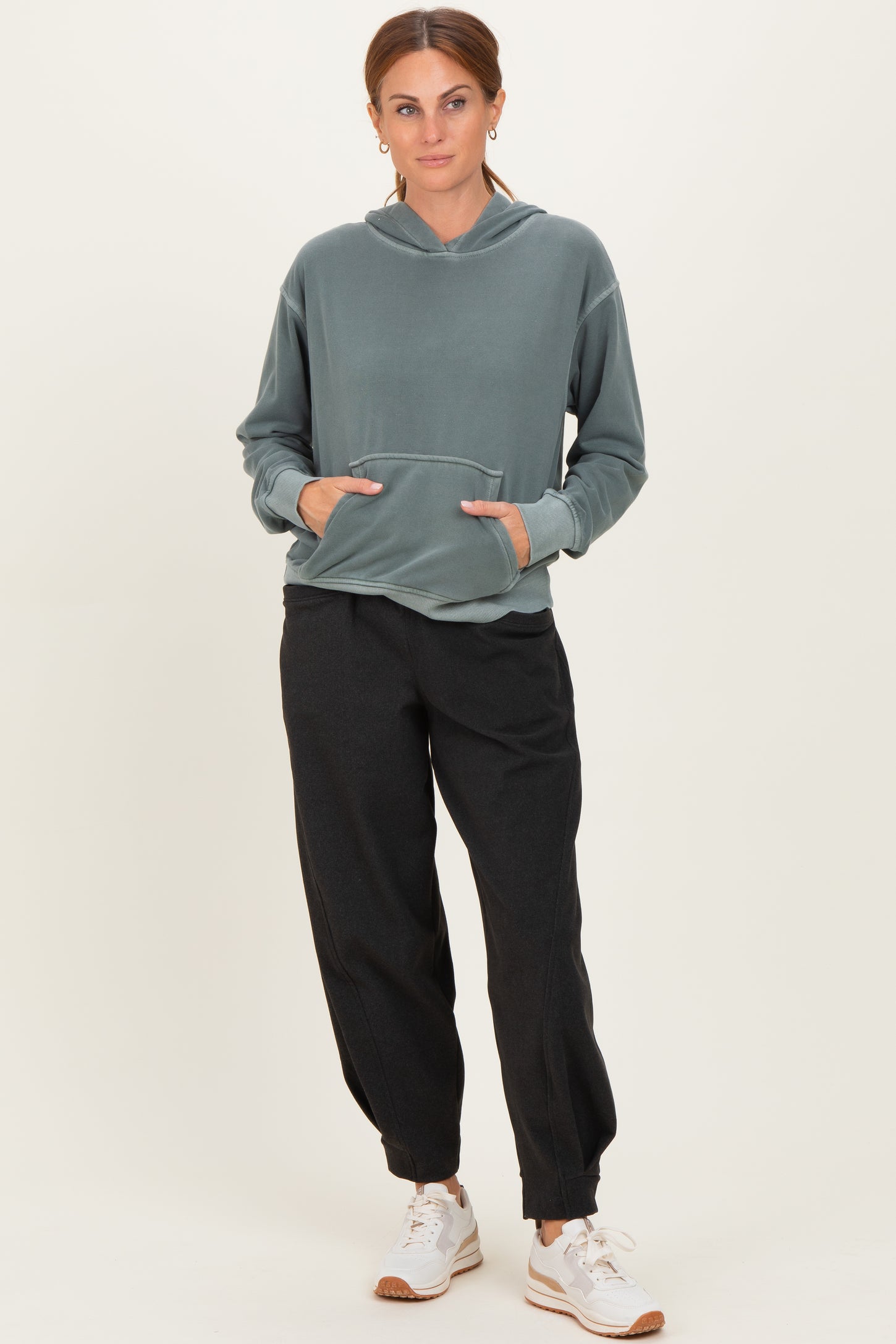 woman wearing a green hooded sweatshirt with a front pocket and black jogger pants, paired with white sneakers
