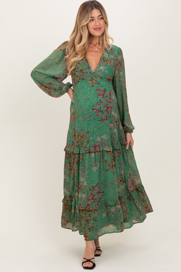 woman wearing a green floral maxi maternity dress with long sleeves and a v-neckline, smiling and standing gracefully