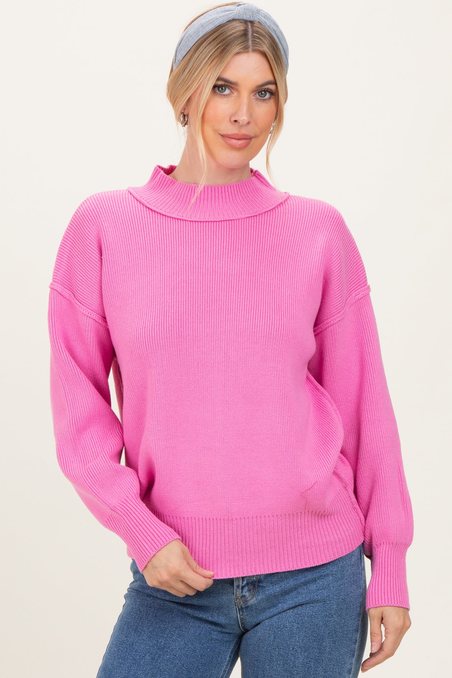 woman wearing a bright pink ribbed sweater with a high neckline and relaxed fit, styled with denim jeans