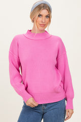 woman wearing a bright pink ribbed sweater with a high neckline and relaxed fit, styled with denim jeans