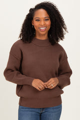 woman wearing a brown oversized sweater with a ribbed neckline and cuffs, smiling at the camera