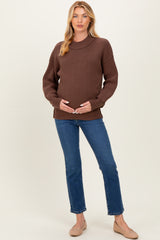 woman wearing a brown maternity sweater and blue jeans, holding her baby bump