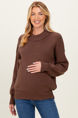 woman wearing a brown maternity sweater with a relaxed fit and long sleeves, holding her baby bump
