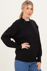 woman wearing a black oversized sweater with a round neckline and long sleeves, paired with blue jeans