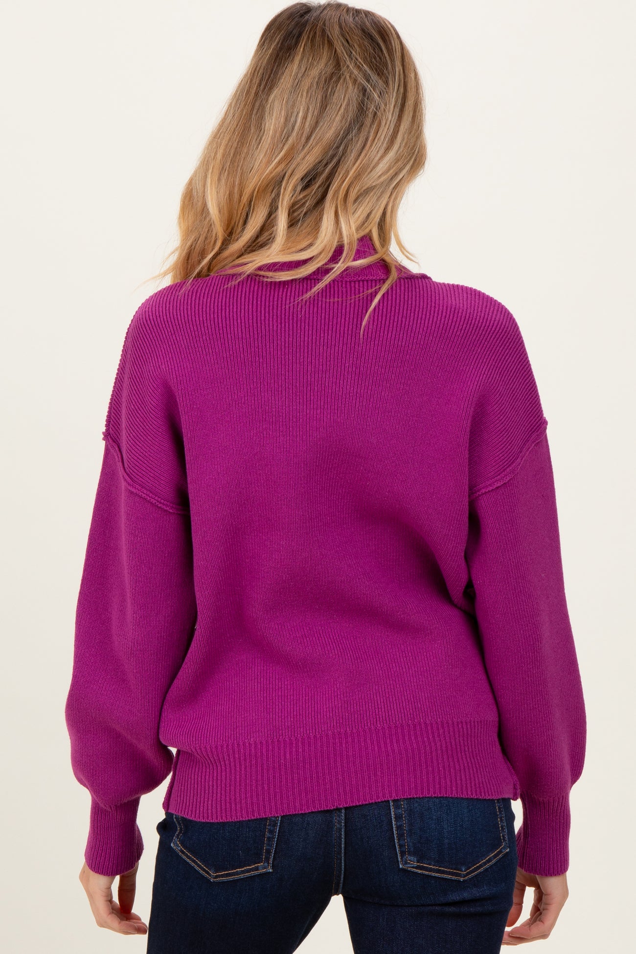 woman wearing a bright pink oversized maternity sweater, viewed from the back, paired with dark jeans