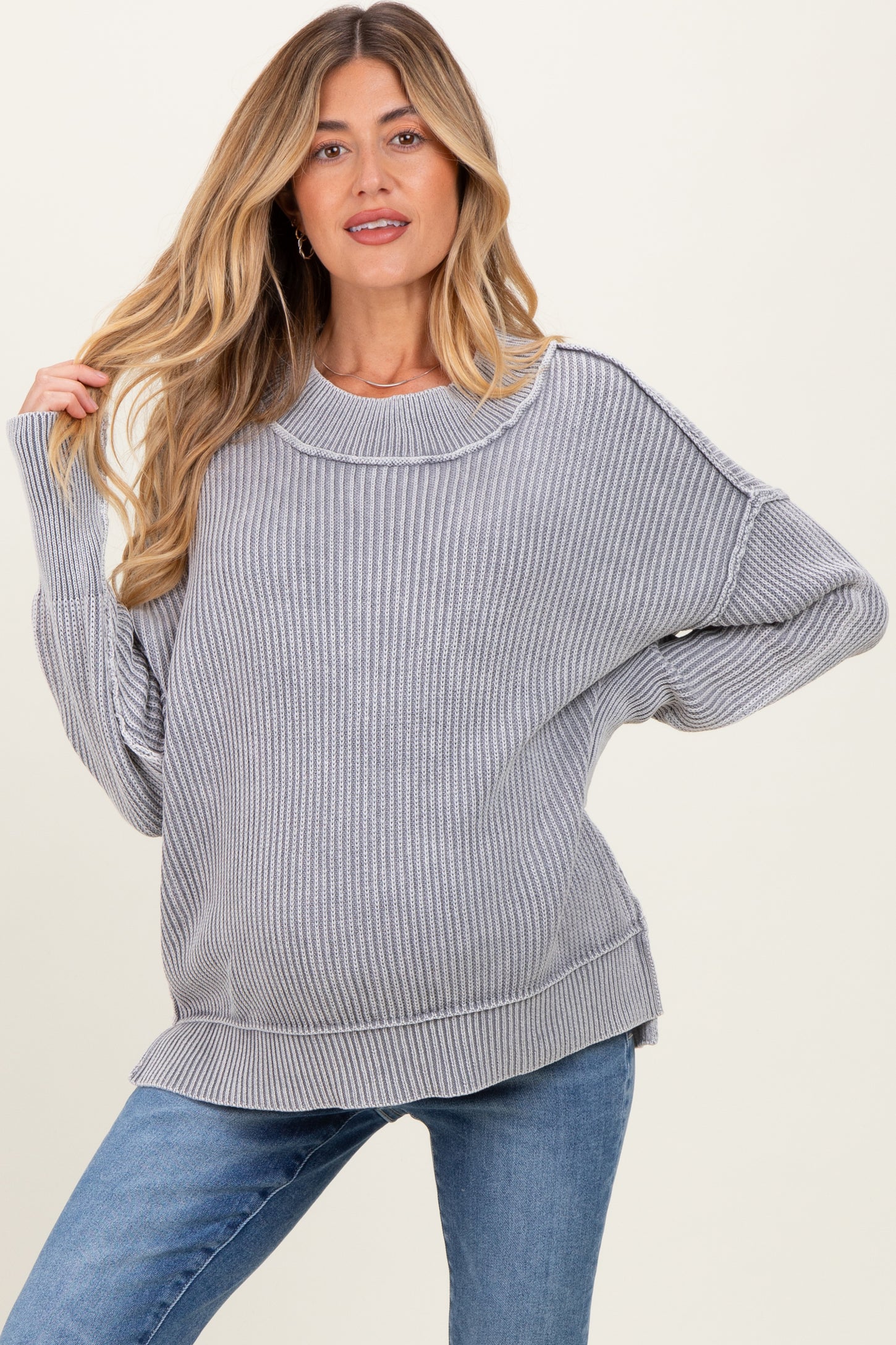 woman wearing a gray ribbed maternity sweater with a loose fit and visible baby bump, paired with blue jeans
