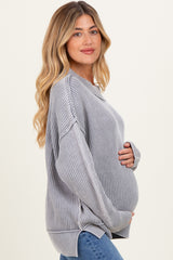 woman wearing a grey oversized ribbed maternity sweater and cradling her baby bump